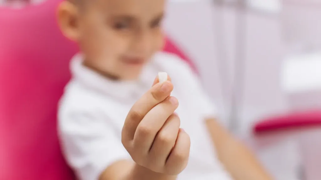 Child smiling while holding an extracted baby tooth after a gentle tooth extraction in Dubai