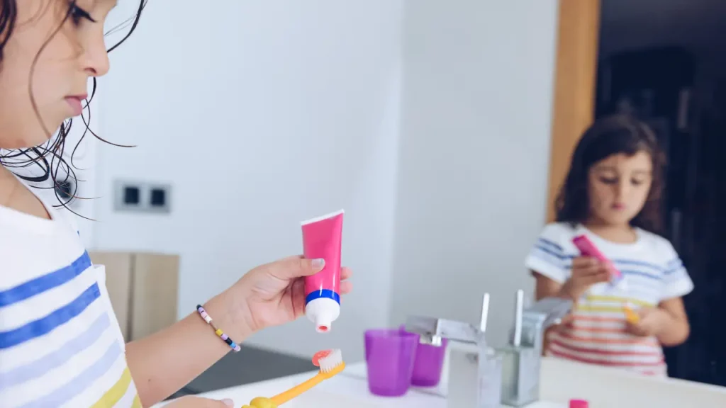Child applying fluoride toothpaste to a toothbrush for daily brushing