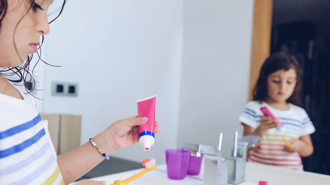 Child applying fluoride toothpaste to a toothbrush for daily brushing