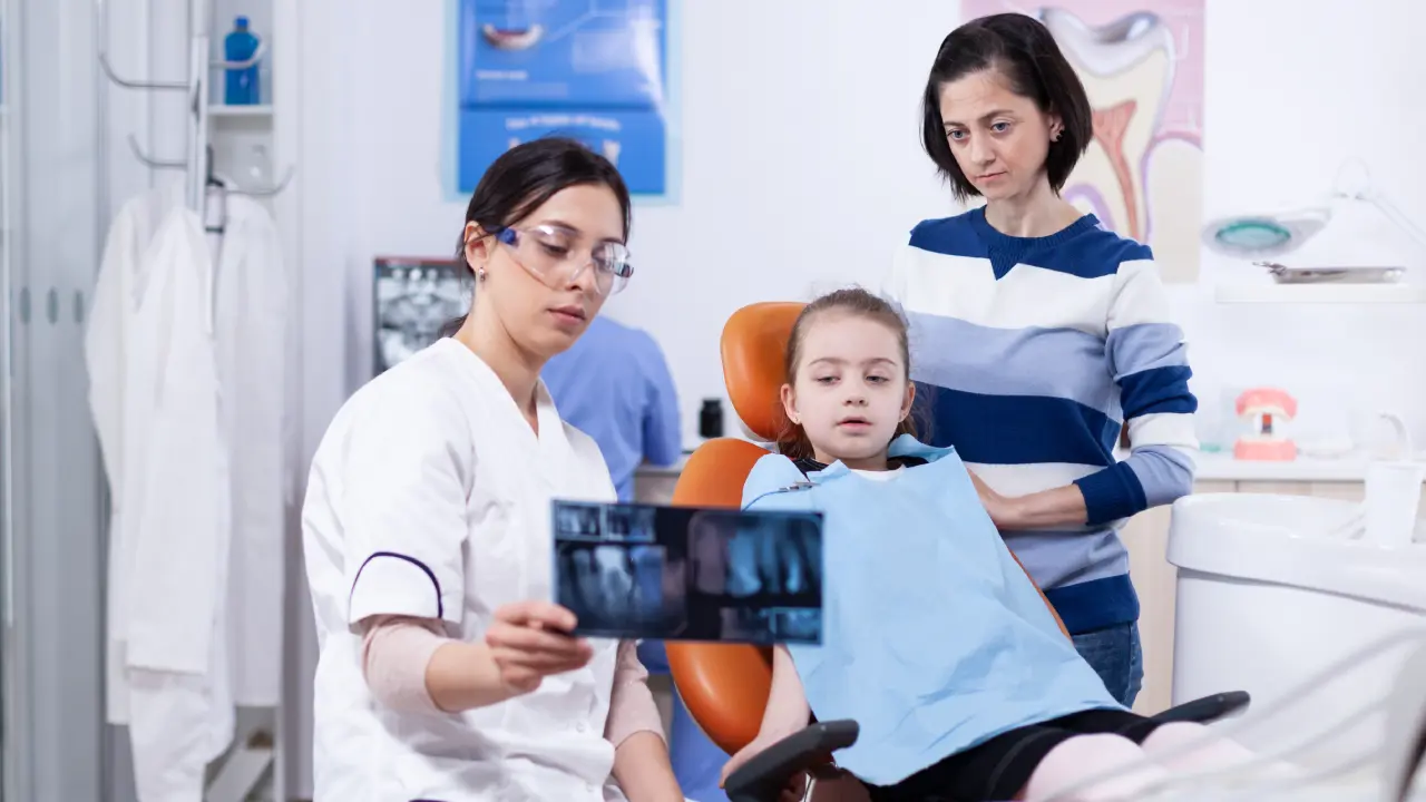 Child undergoing a dental examination while a dentist reviews an X-ray with a parent